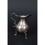 A George II silver cream jug with wavy rim edge on three paw feet,