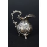 A small continental silver cream jug with embossed floral decoration on three legs,