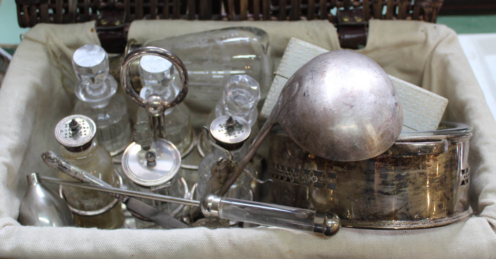 A basket containing silver plated six bottle cruet plus other silver plated wares