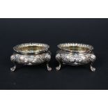 A pair of Victorian silver salts with embossed floral detail on three paw feet by Robert Harper,