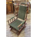 An Edwardian green velvet upholstered American rocking chair with turned arms and back