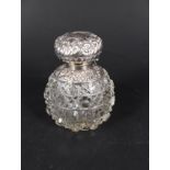 A silver lidded cut glass perfume bottle, the lid with embossed floral decoration,
