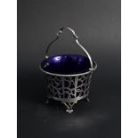 A pierced silver sugar basket with blue glass liner on four feet with swing handle