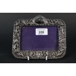 A silver photograph frame with pierced and embossed floral and bird decoration by William Comyns,