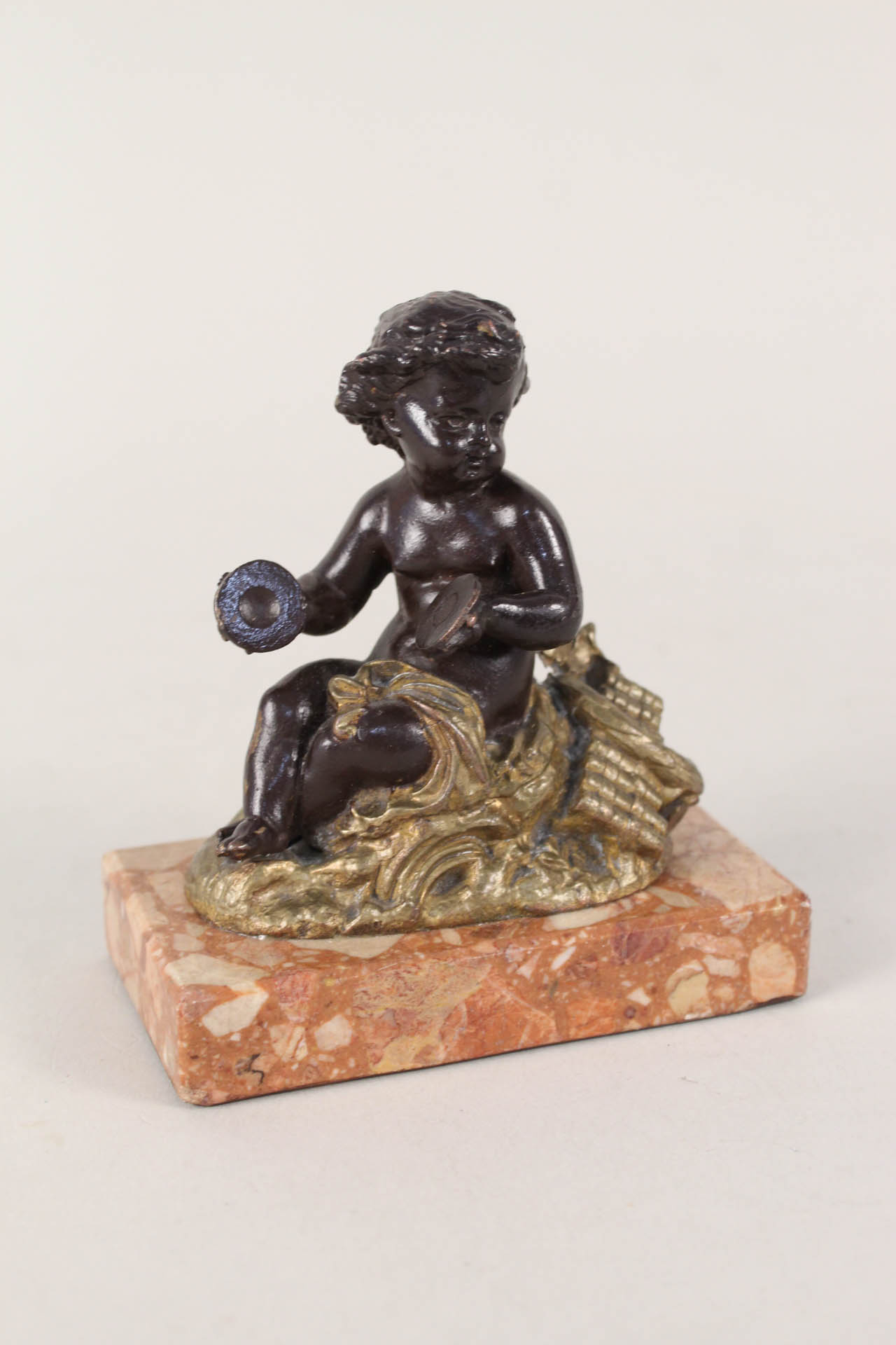 A bronzed and gilt metal seated putto on variegated marble base,