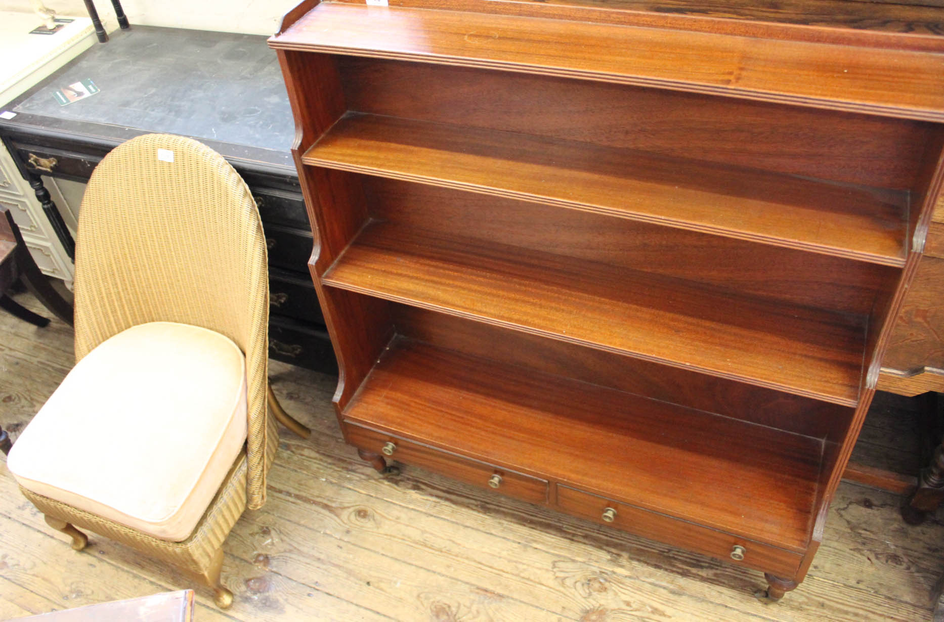 A Lloyd Loom gold chair and a reproduction bookcase with two drawers on castors