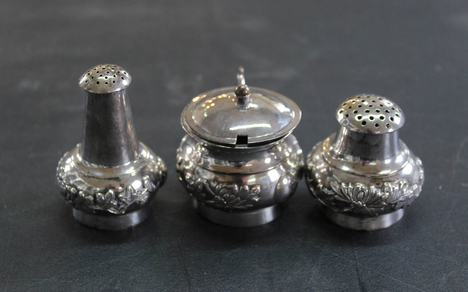 An oriental white metal three piece set cruet decorated with flora,