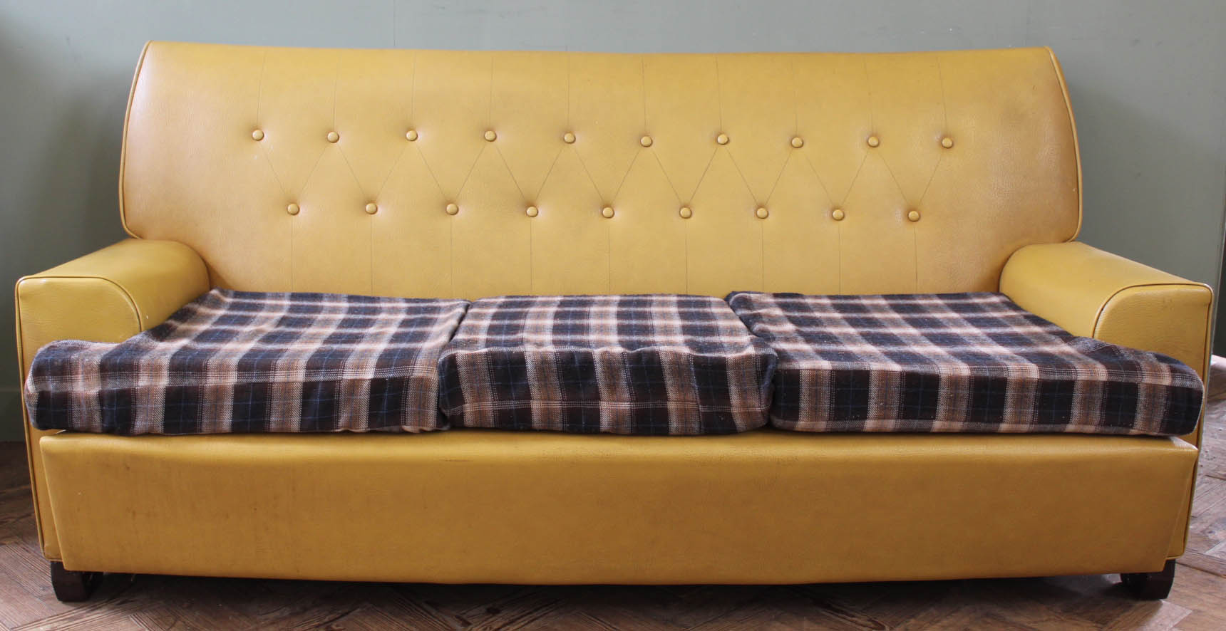A 1960's mustard vinyl button back sofa with checked seat cushions