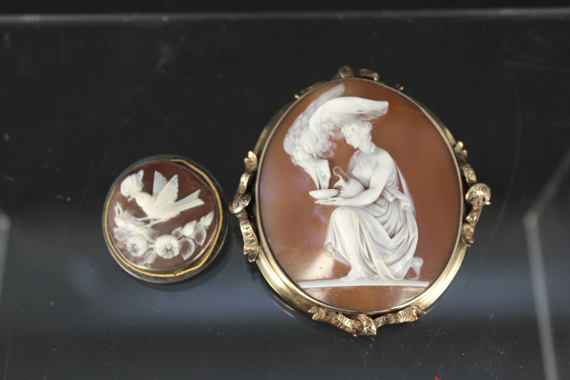 A large yellow metal framed shell cameo brooch together with a smaller white metal framed brooch