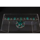 A large silver floral shaped brooch set with multiple green stones and a similar silver bracelet