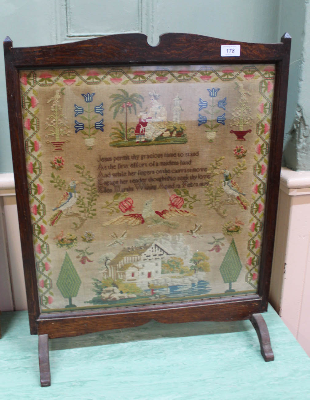 An oak fire screen containing woolwork motto, house and bird sampler by Martha Whiting, aged 12,