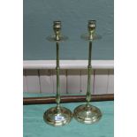 A pair of tall Edwardian brass candlesticks with drip trays, slender stems and circular bases,