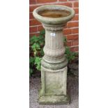 A weathered concreted bird bath on column and square plinth base