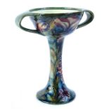 A William Moorcroft two handled pedestal cup, decorated with the Spanish pattern, on a mottled green