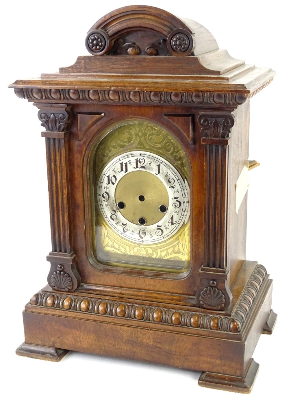 An early 20thC German walnut mantel clock, with arched engraved dial, silvered chaptering and carved