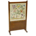 An early 20thC oak fire screen, with a crewel work insert, decorated with a squirrel, stag,