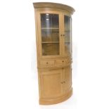 A light oak corner cabinet, the top with a moulded cornice, with two glazed doors enclosing glass