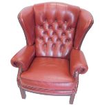 A red leather upholstered wingback chair in George III style, with studded borders and channelled
