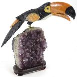An exotic hardstone model of a Toucan, standing on an amethyst crystal base with separate plinth,