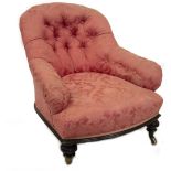 A Victorian low armchair, upholstered in pink buttoned damask, and having ebonised frame with carved