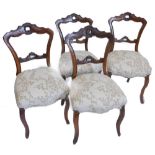 A set of four Victorian walnut balloon back chairs, each with a pierced back, padded seat, on