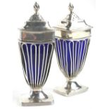 A pair of George V silver pepper pots, each of rectangular urn form, pierced sides and blue glass
