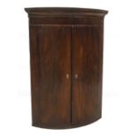 A George III mahogany hanging bowfront corner cupboard, with moulded cornice over two doors, with