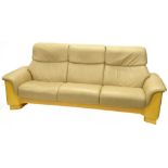 A Stressless cream leather three seat sofa, with satin birch veneered ends, etc., stamped Ekrones.