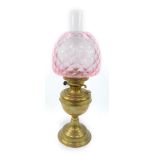 An early 20thC brass oil lamp, with a glass chimney and pink honeycomb glass shade, 53cm H.