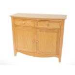 A light oak bow front sideboard, with two drawers over a pair of cupboard doors, raised on square