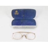 A pair of pince-nez spectacles, with yellow metal expanding nose bridge frame, in an aluminium