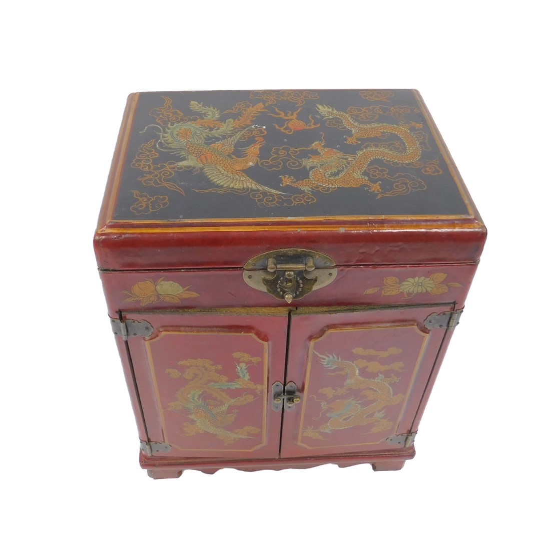 A 20thC Chinese red lacquer table cabinet, decorated with figures at a table, dragons and birds, the