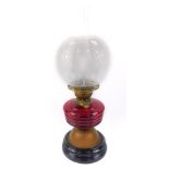 An early 20thC brass table lamp, with a turned ruby glass reservoir, raised on a black ceramic socle