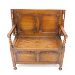 An early 20thC oak monks bench, with a plain top and panelled back, arms with bobbin turned