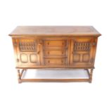 A Reprodux oak sideboard, with a pair of paneled doors flanking three drawers, raised on turned
