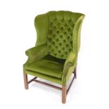 A George III style mahogany wingback armchair, upholstered in button back green draylon, raised on