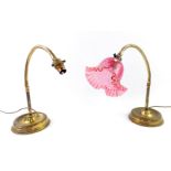 A pair of brass anglepoise lamps, one with a frilled cranberry glass shade, raised on turned
