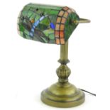 A brass desk lamp, with Tiffany style stained glass shade, decorated wit a dragon fly etc., on a