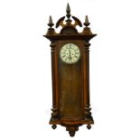 A late 19th/early 20thC walnut cased Vienna wall clock, the shaped crest with three turned finial's,