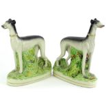 A pair of Staffordshire style pottery figures of standing grey hounds, in naturalistic settings,