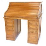 An early 20thC oak roll top desk, the tambour front enclosing a fitted interior above four drawers