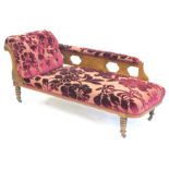 A late Victorian carved oak chaise lounge, upholstered in textured deep red velvet on turned legs.