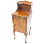 An early to mid 20thC walnut bedside cabinet, with a raised back above a slide and a door on