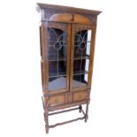 A carved oak display cabinet, with a moulded cornice above two leaded glazed doors, and frieze