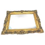 A gilt rectangular wall mirror, with a bevelled plate and a frame decorated with swags, scrolls etc.