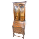 An early 20thC oak bureau bookcase, the top with two leaded and part stained glass doors, above a