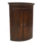 A George III mahogany hanging bowfront corner cupboard, with moulded cornice over two doors, with