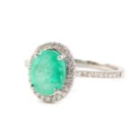 An 18ct white gold emerald and diamond ring, the oval cut emerald in a surround of diamonds, the