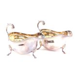 A pair of silver sauce boats, with a gadrooned rim and scroll handle, raised on three hoof feet,