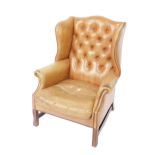 A Georgian style mahogany wing back club armchair, upholstered in button back tan leather, with